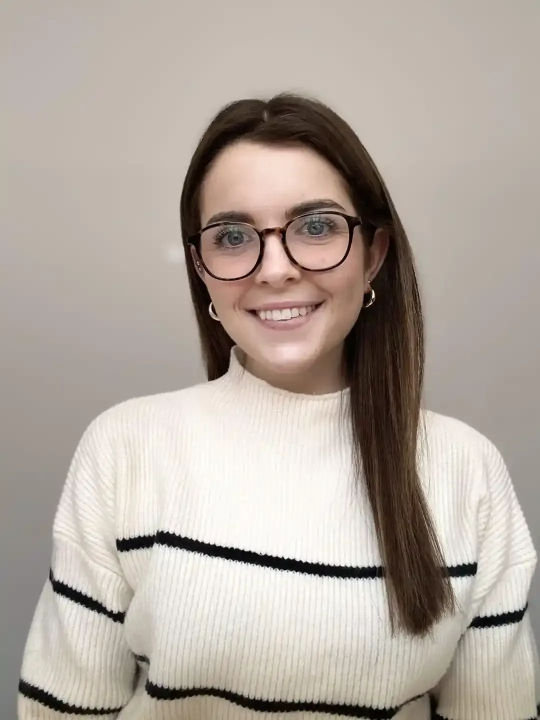 Woman with glasses smiles, wearing a white sweater with black stripes.