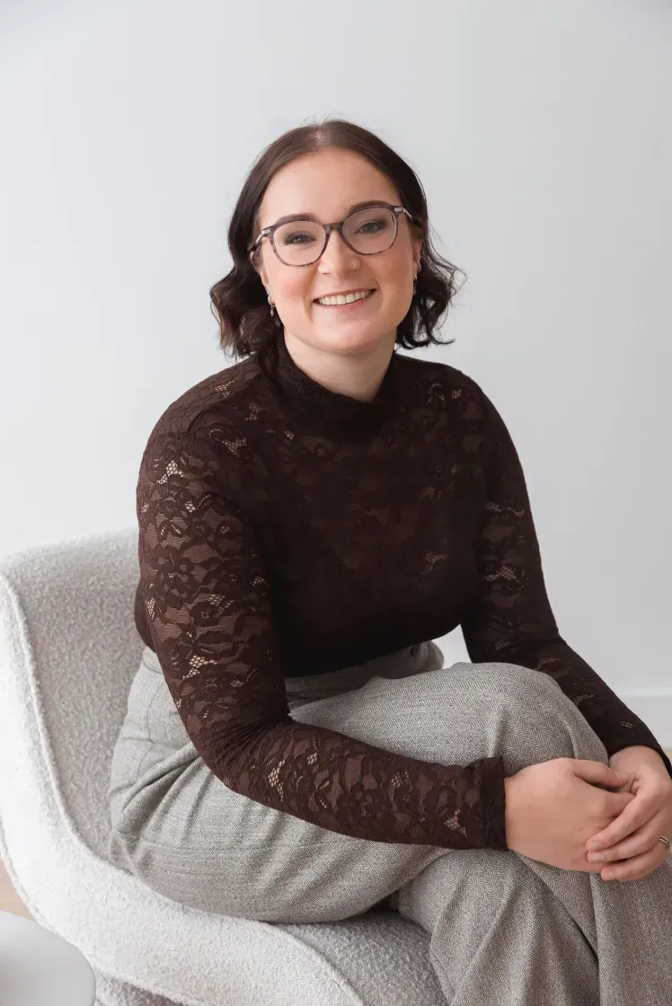 Woman in a Brown Tops smiles while seated in a gray armchair.