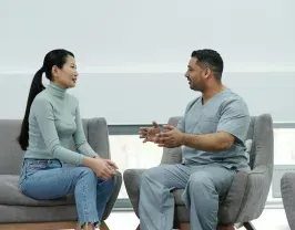 Woman in jeans and a sweater chats with a person in scrubs in a waiting room.