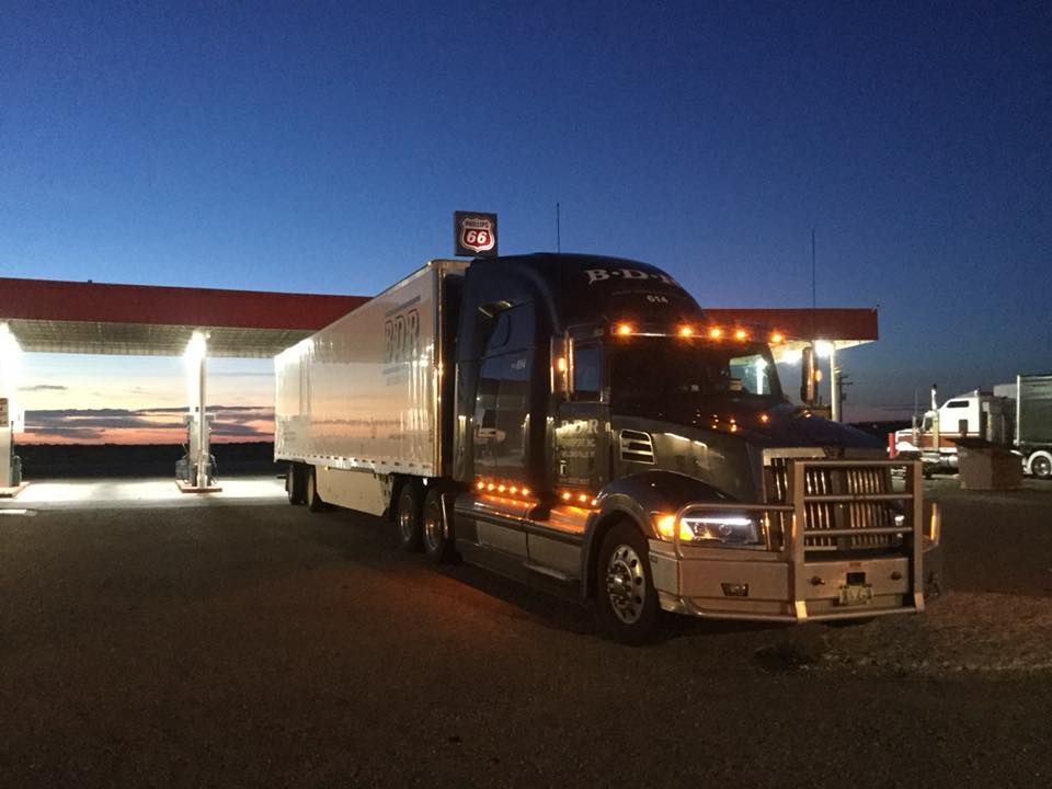 A semi truck is parked in front of a gas station at night.