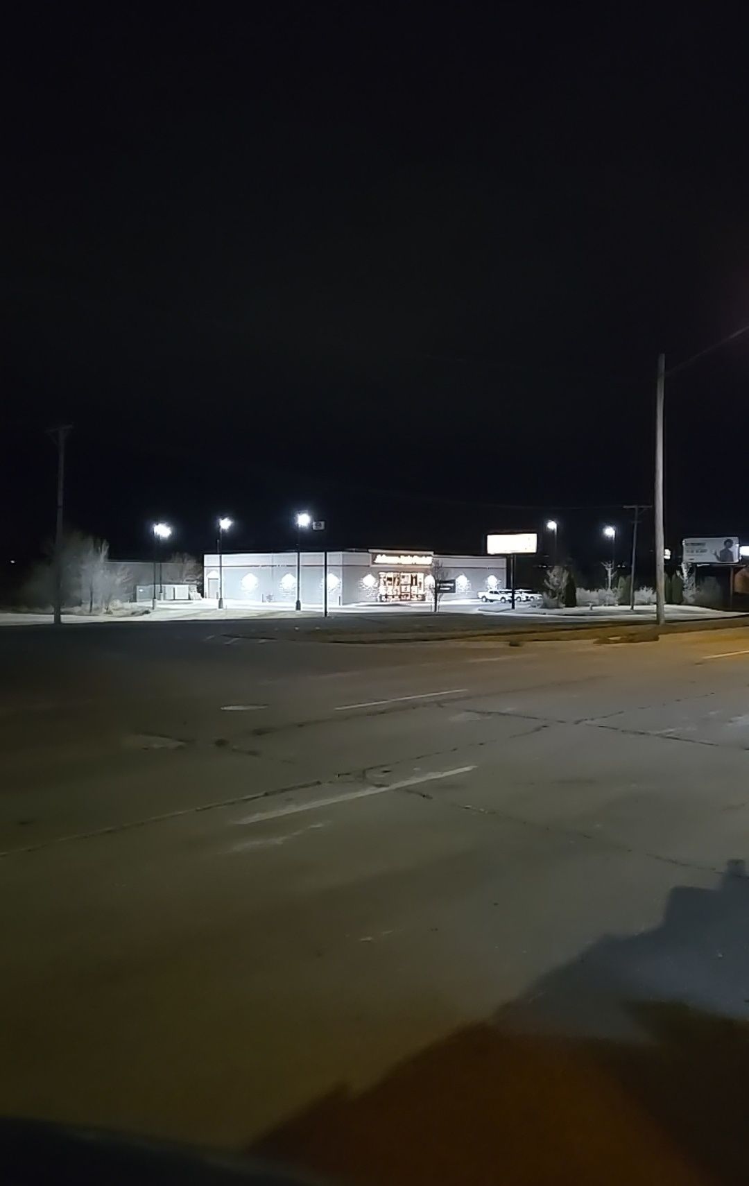A lit up store building at night with a mostly empty parking lot in front.