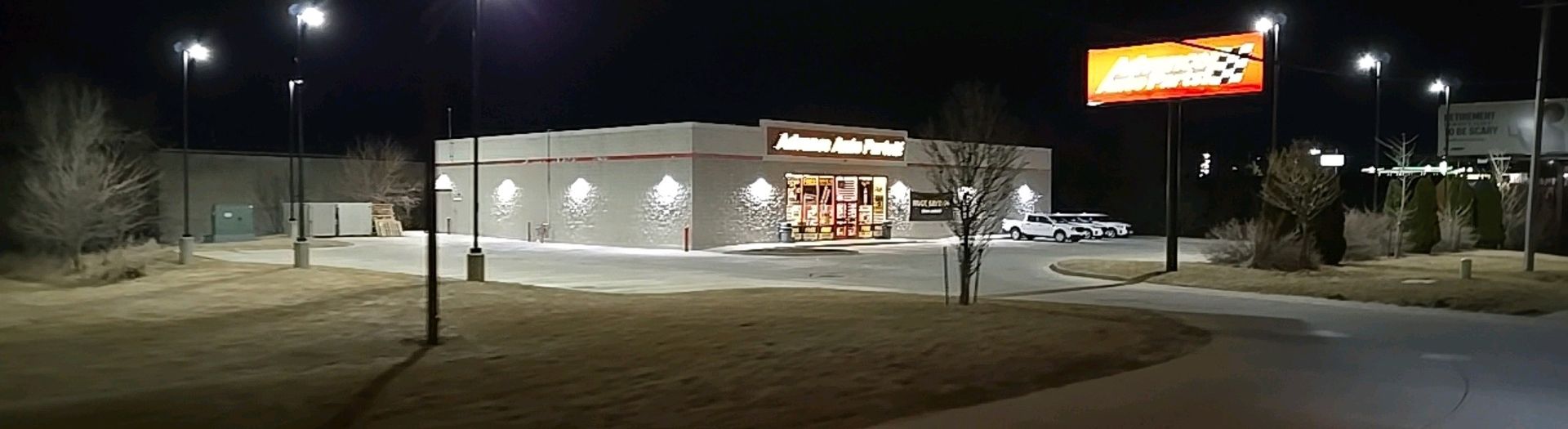 Nighttime exterior of a business: brown building with sign and parking lot, lit streetlights in view.
