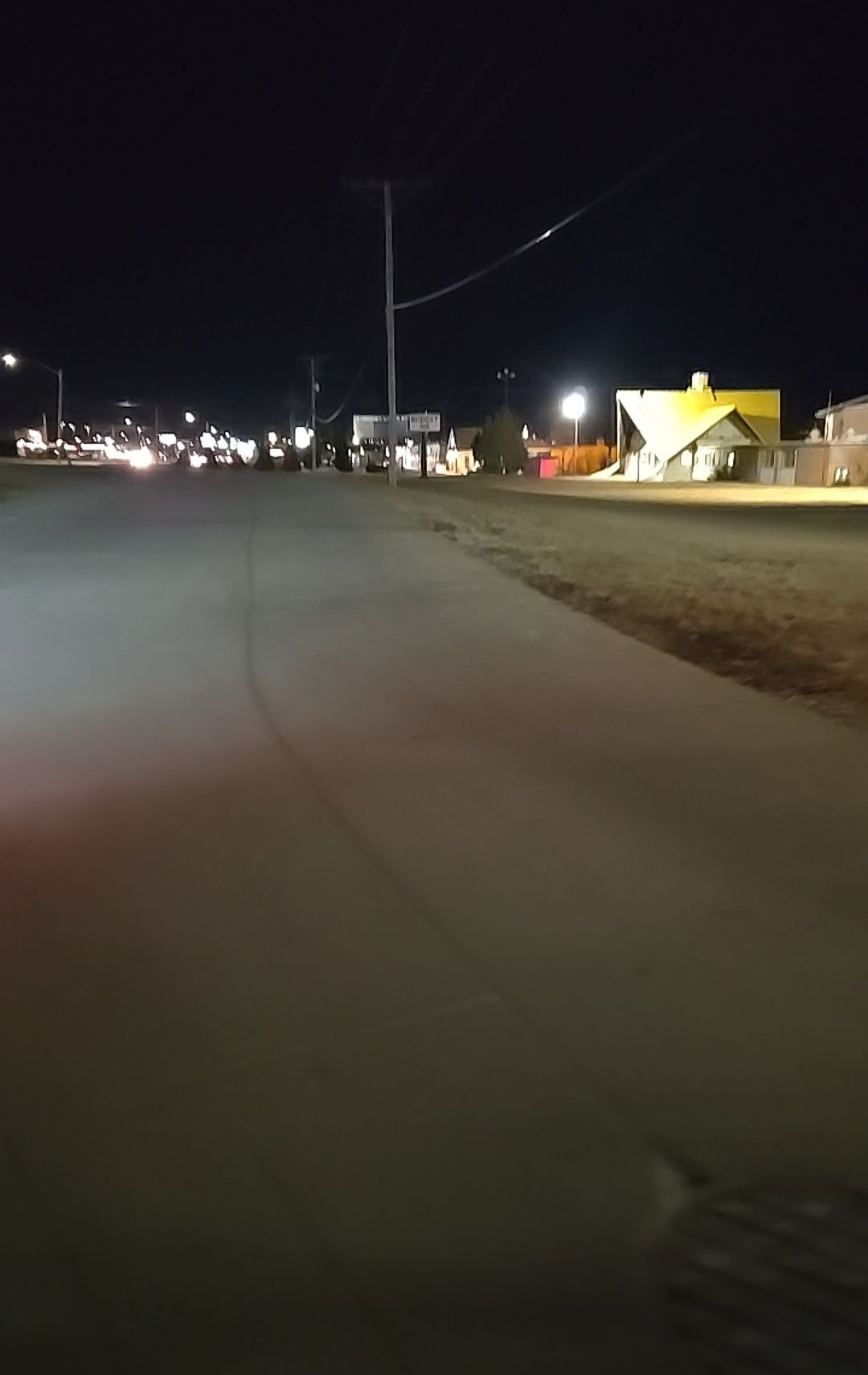 Nighttime street scene with road, sidewalks, and buildings lit by streetlights.