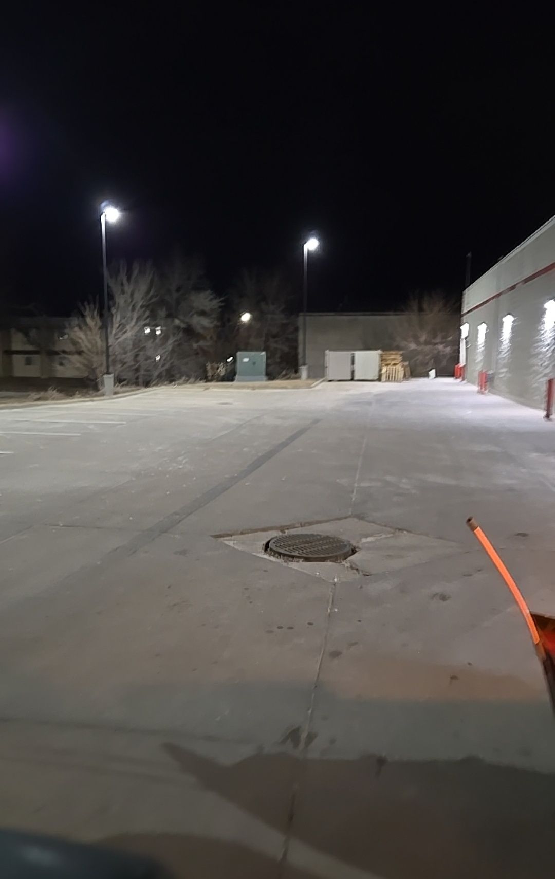 Nighttime view of a snow-covered parking lot with streetlights and a building on the right.