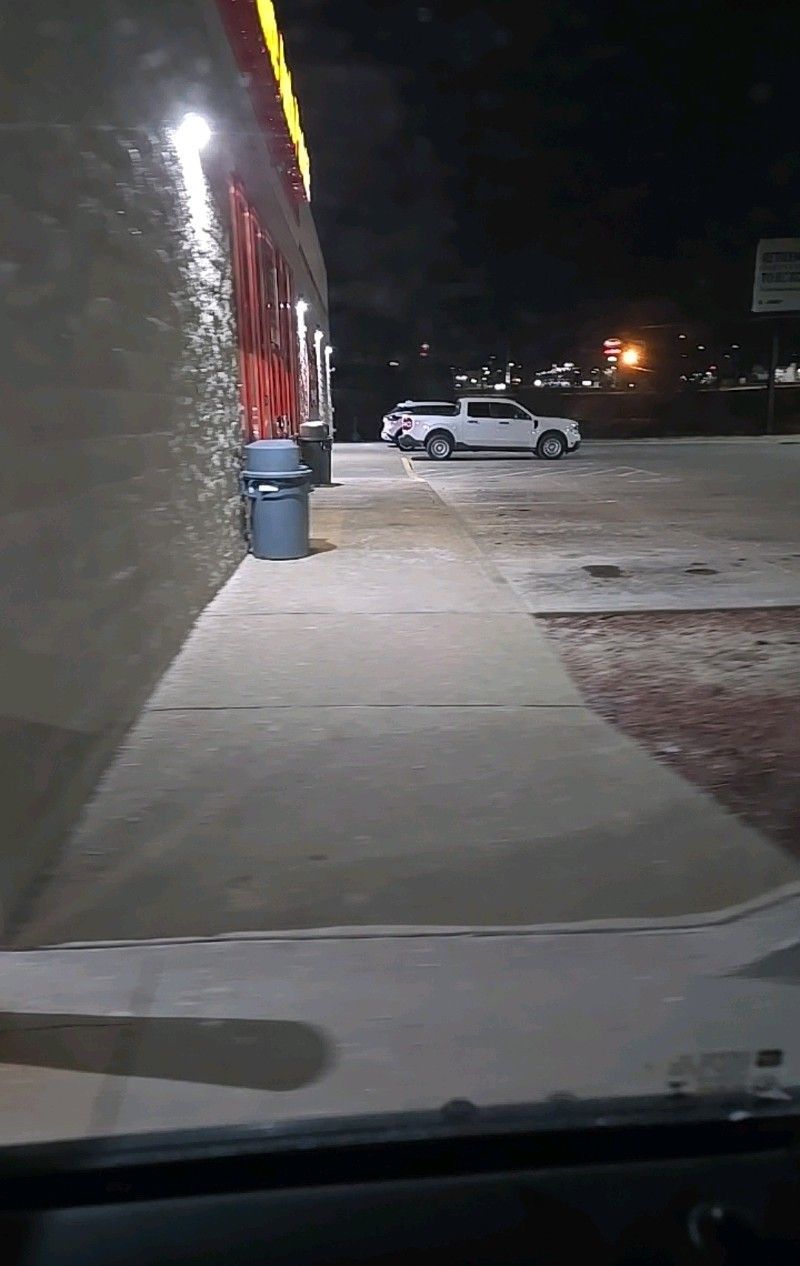 Nighttime exterior shot of a building with bright lights. A white pickup truck is parked in front of the building.