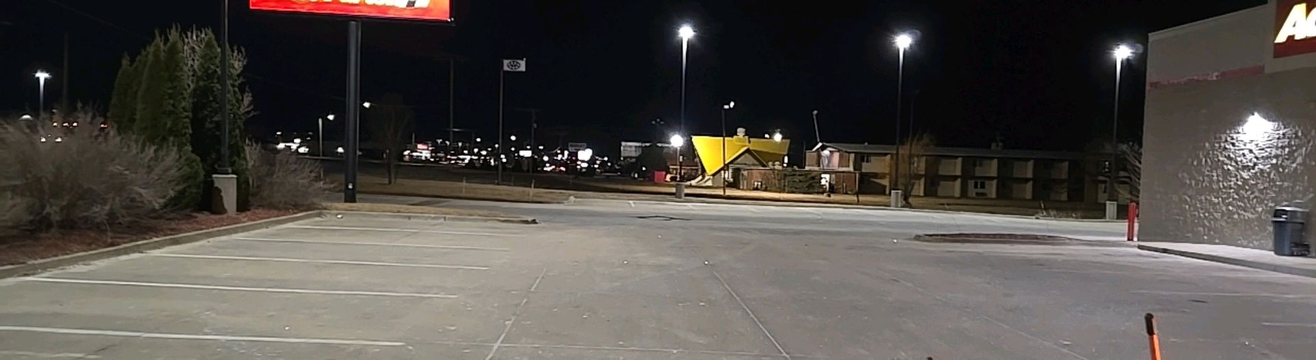 Nighttime parking lot with streetlights, a fast-food restaurant, and distant buildings.
