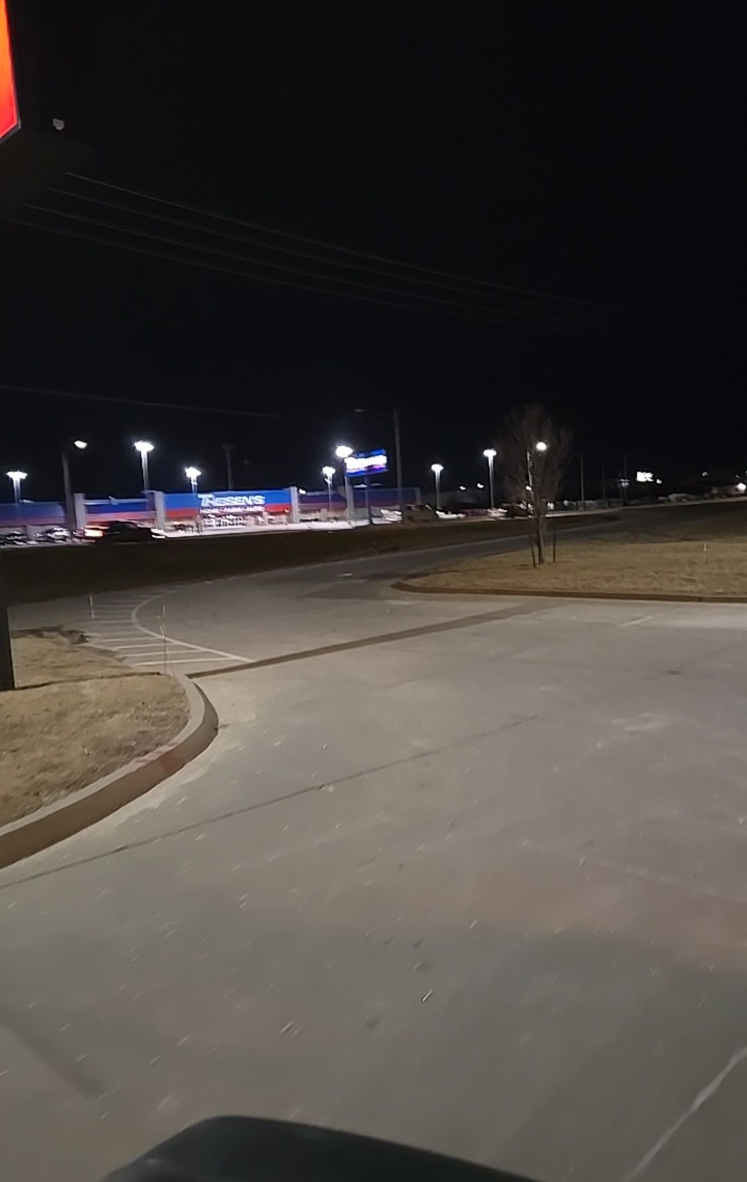 Nighttime scene of a brightly lit commercial area with buildings, streetlights, and a car on the road.