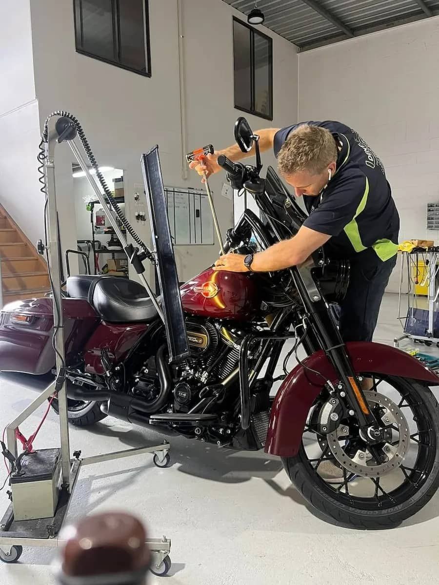 A Man Is Working on A Motorcycle in A Garage — Dent Motive in Helensvale, QLD