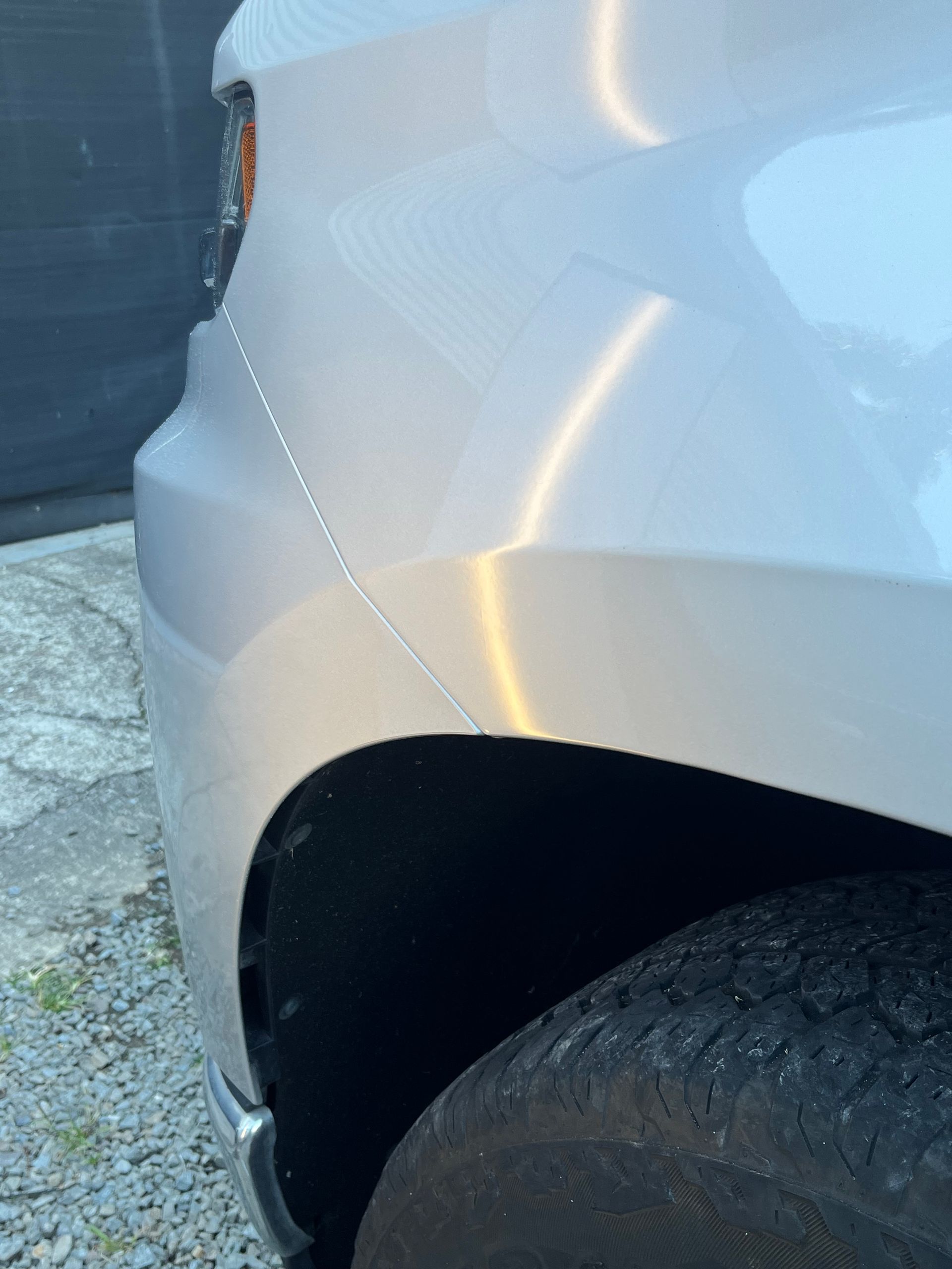 A close up of a car 's fender and tire on a gravel road.