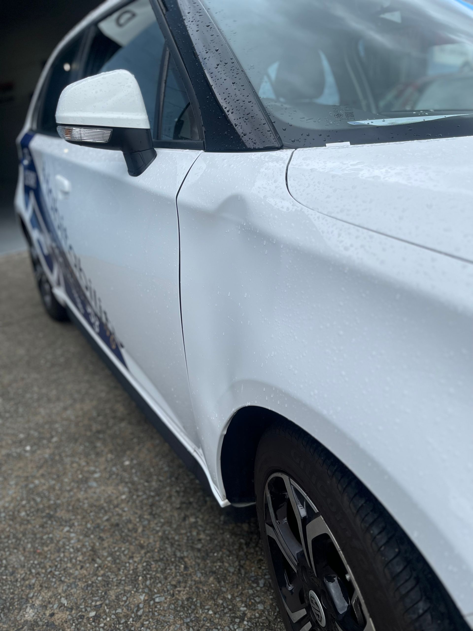 A white car with a damaged fender is parked in a garage.