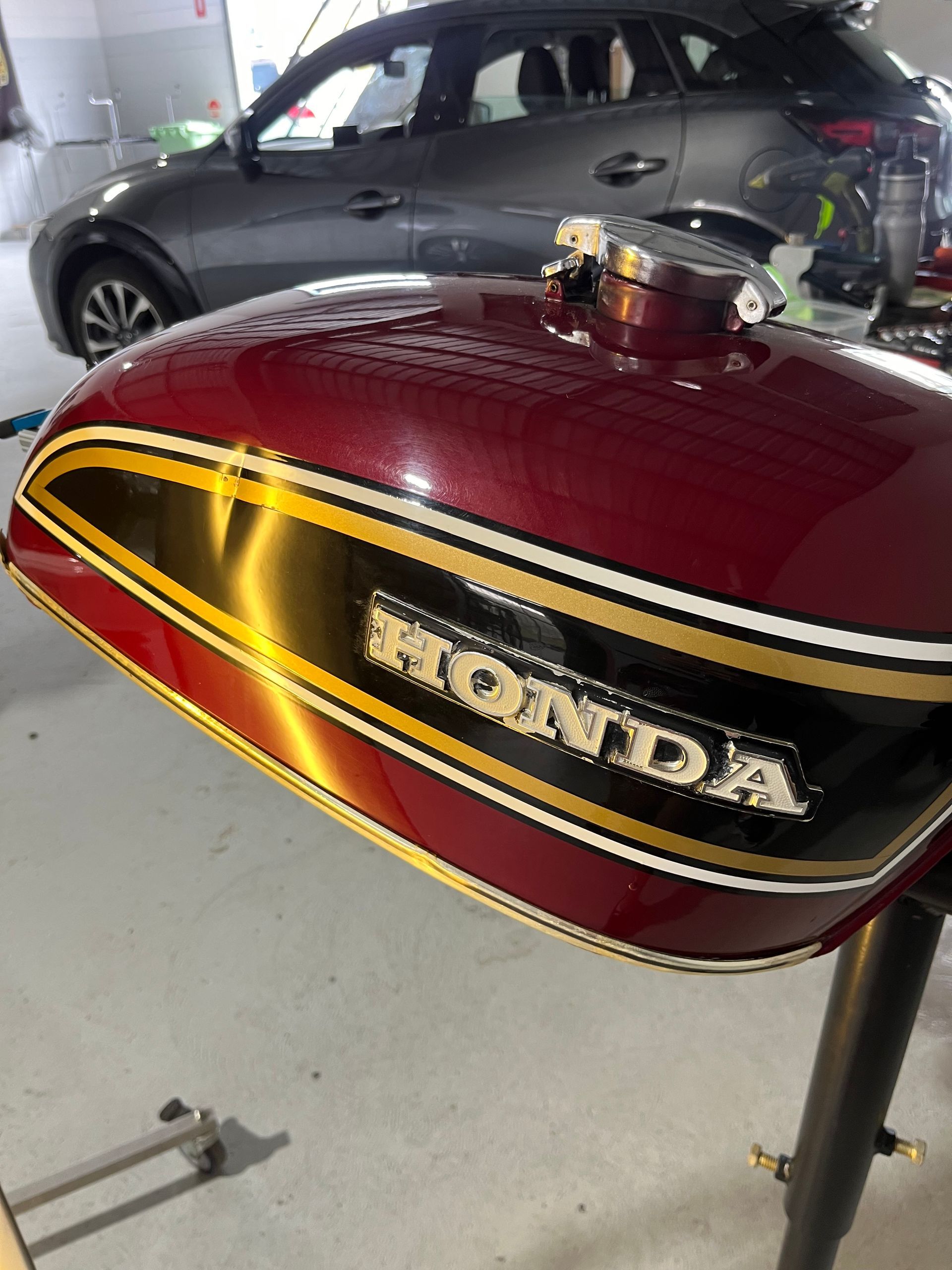A red honda motorcycle tank is sitting in a garage next to a car.
