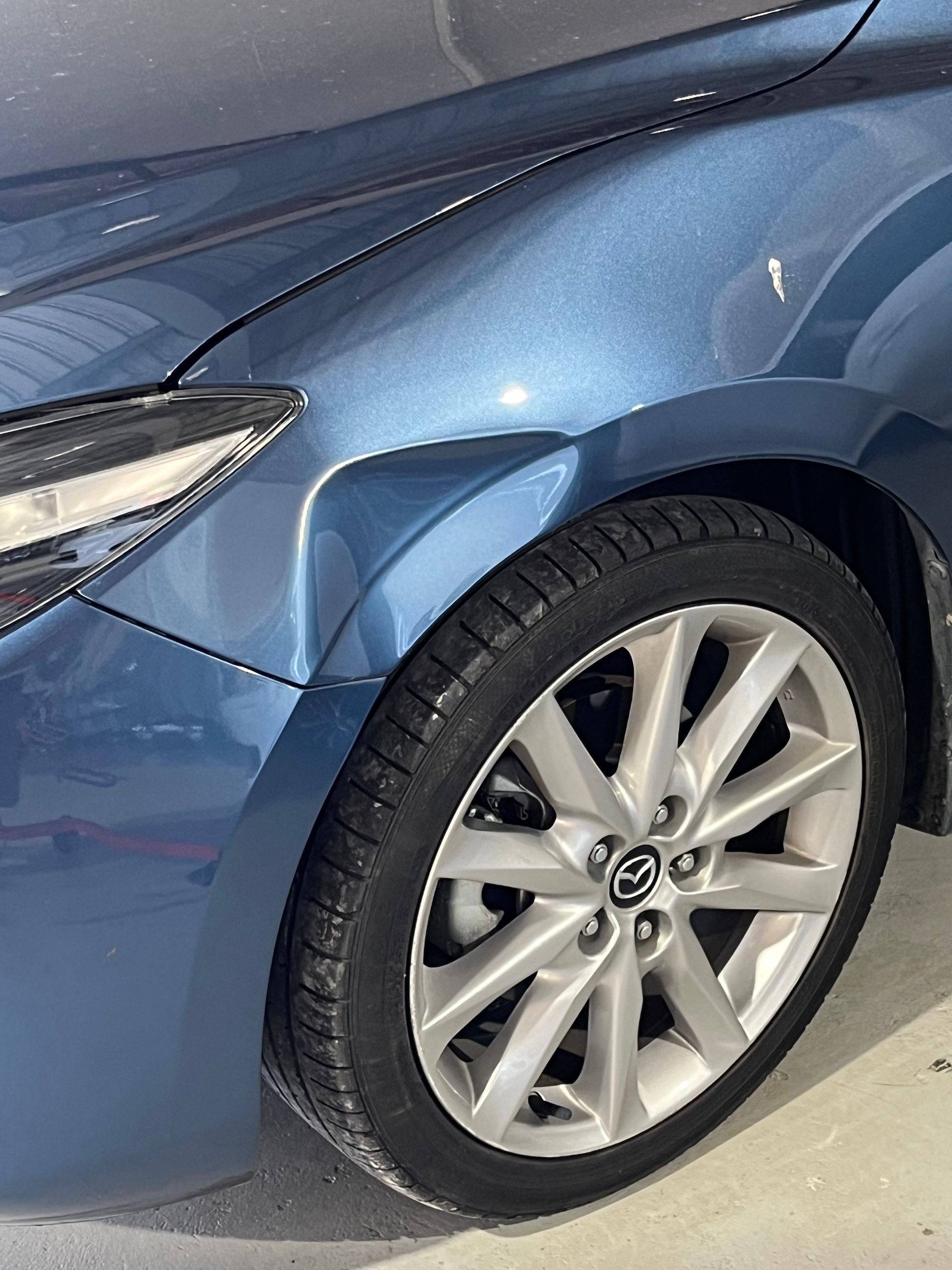A blue car with a damaged fender is parked in a garage.