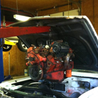 A red automotive engine being hoisted by a red engine crane inside a garage.