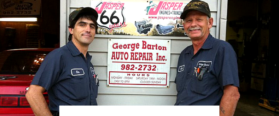 Two auto mechanics in blue uniforms stand smiling in front of a shop sign for George Barton Auto Repair Inc.