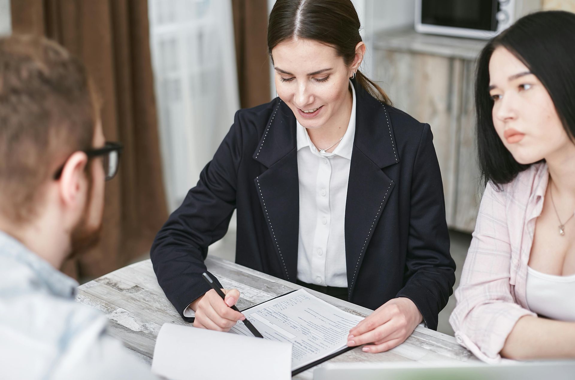 Woman in blazer reviews paperwork with a couple at a table.