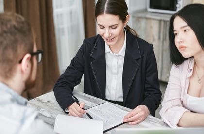 Woman in blazer reviews paperwork with a couple at a table.