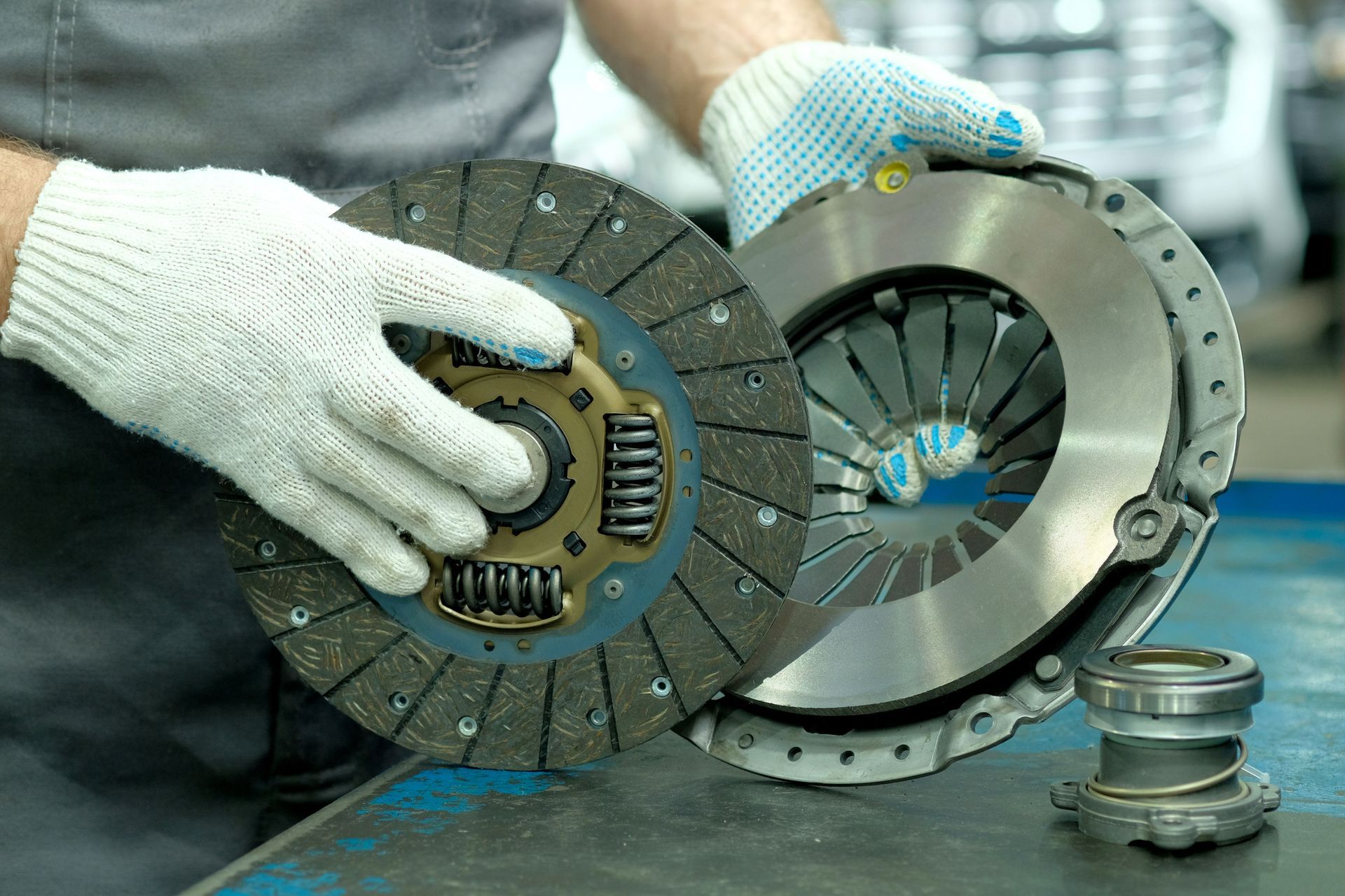 A man wearing gloves is holding a clutch disc on a table.