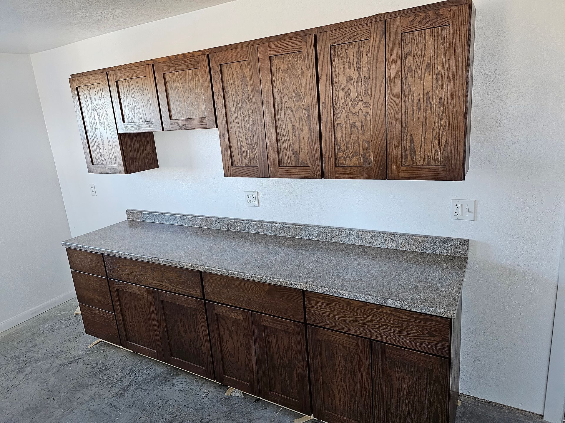 Dark wood kitchen cabinets with a gray speckled countertop against a white wall.