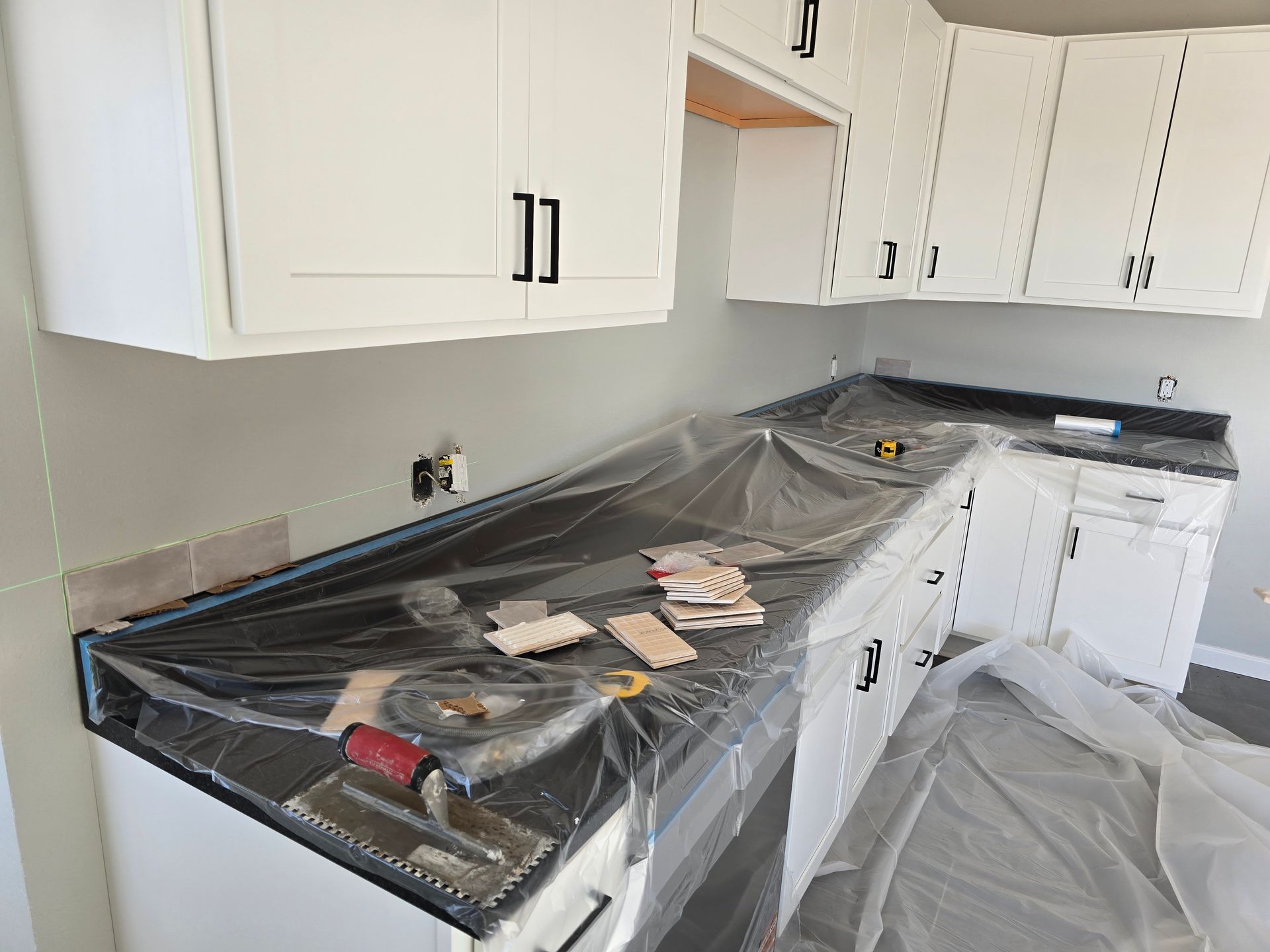 Kitchen renovation with cabinets, countertop covered with plastic, and tools on the counter.