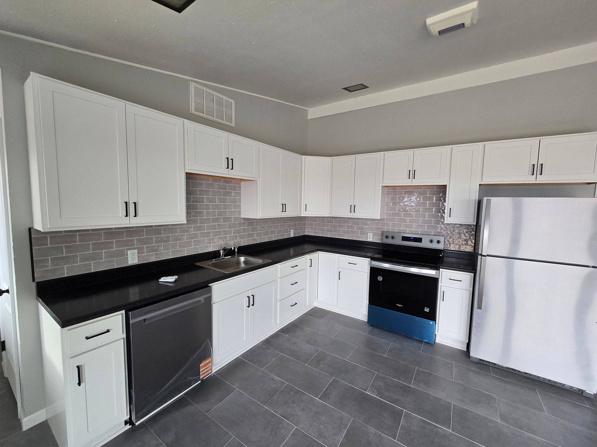 White kitchen cabinets with black countertops and gray tile backsplash.