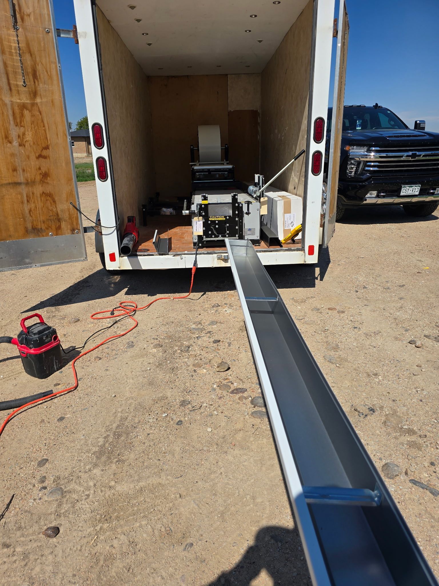 Gutters extending from a trailer; a machine inside appears to make them. A truck is parked to the right.