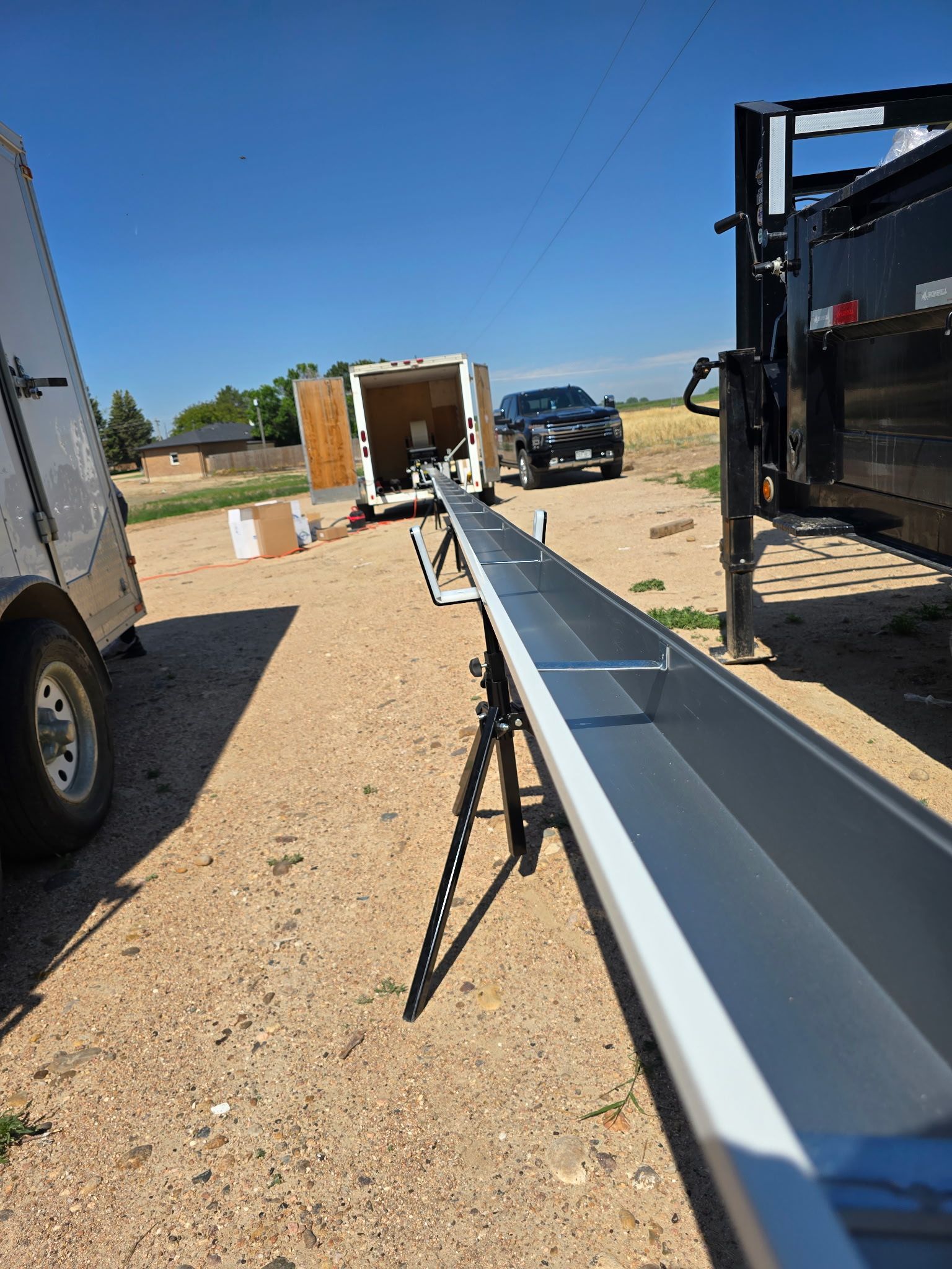 Long metal gutter on a tripod. Trailers and truck are in the background, set outdoors on a sunny day.