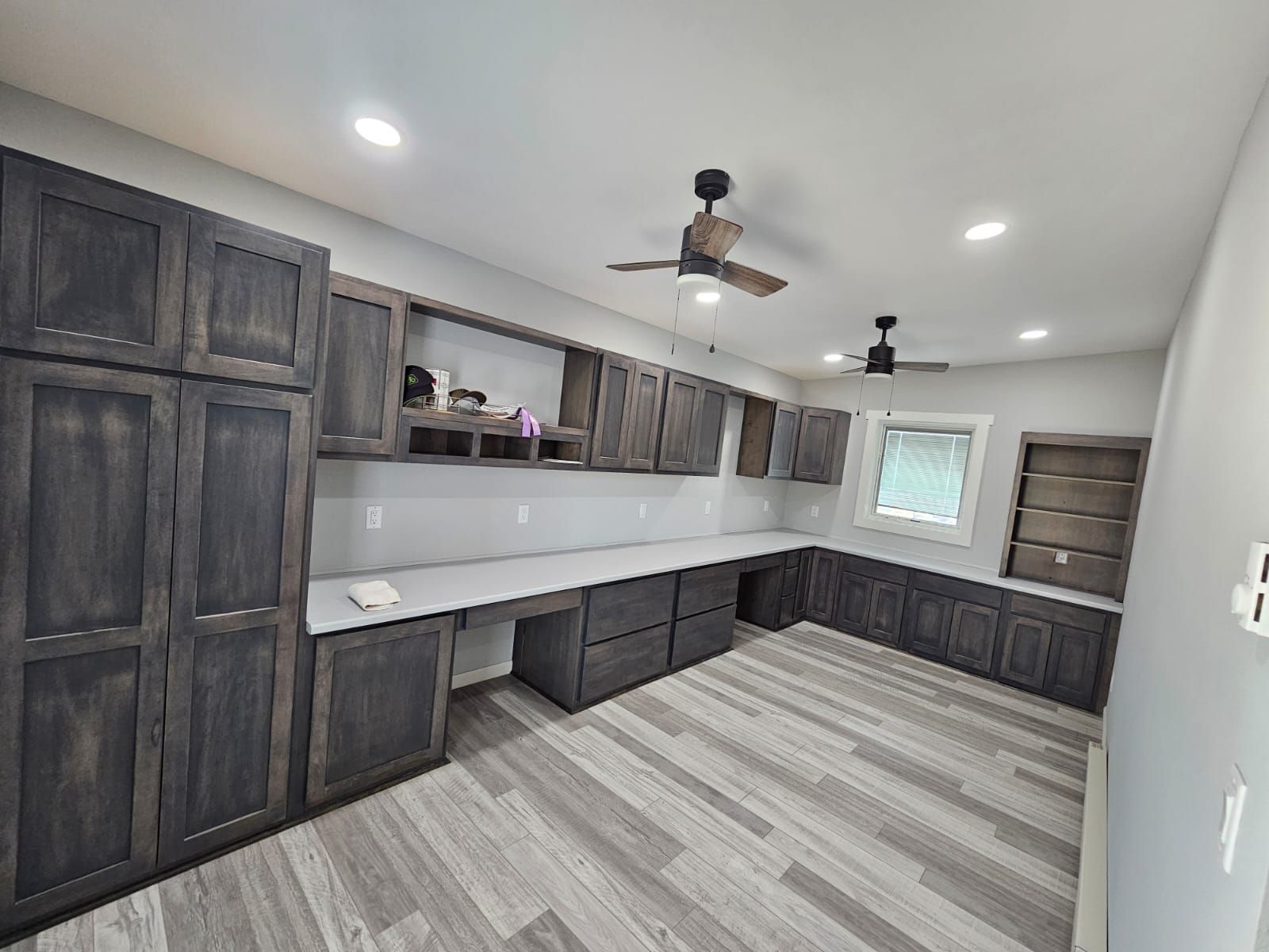 Dark gray cabinets and desk in a room with light gray flooring and a window.
