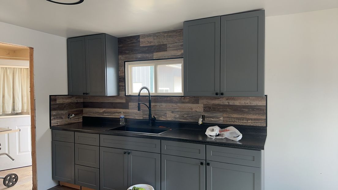 Gray kitchen cabinets and countertops with a black faucet against a wood-look backsplash.