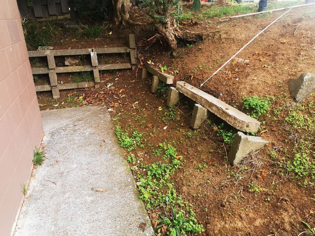 A concrete fence is sitting in the middle of a dirt field next to a sidewalk.