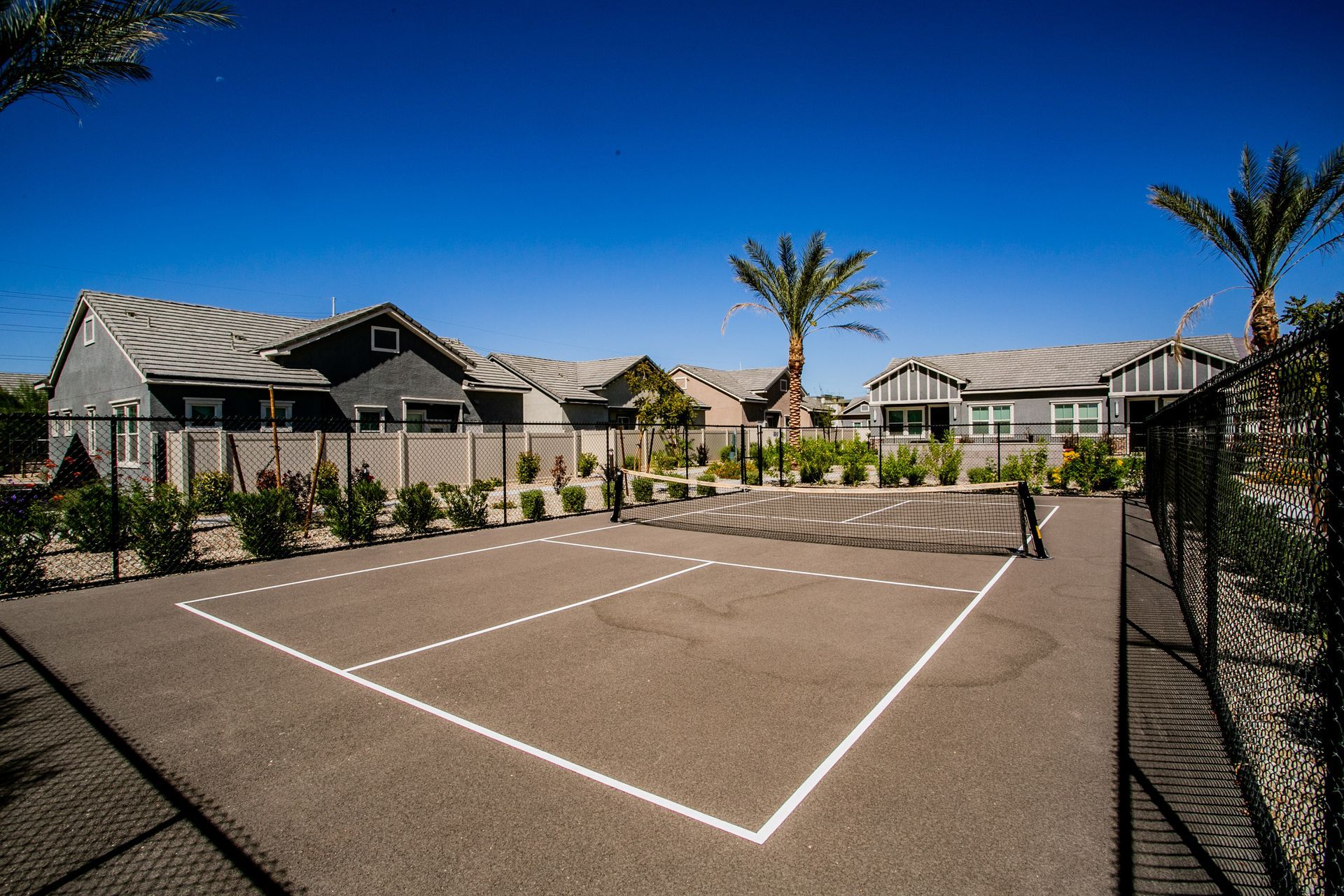 A tennis court in front of a house with palm trees