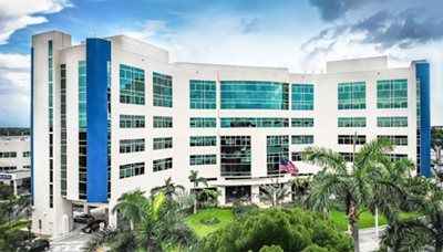 Modern multi-story building with blue accents and large windows, possibly a medical facility.