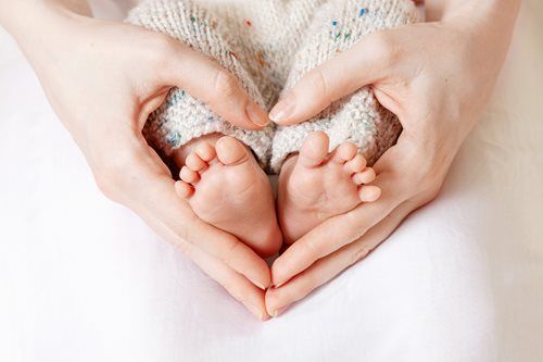 Hands forming a heart around a baby's feet on a soft white blanket