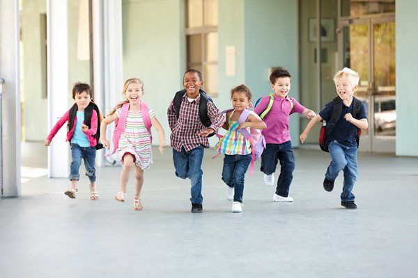 Five children running toward the camera in a bright school hallway