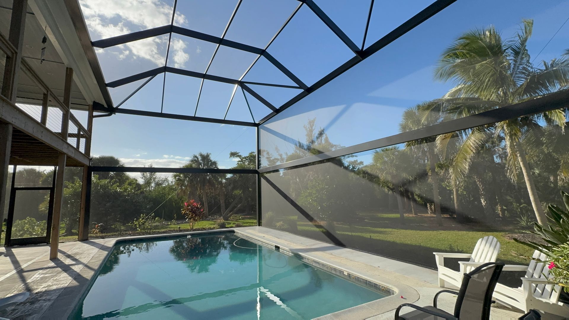 Dark gray pergola over a patio next to a house with a view of a lake and a screened enclosure.