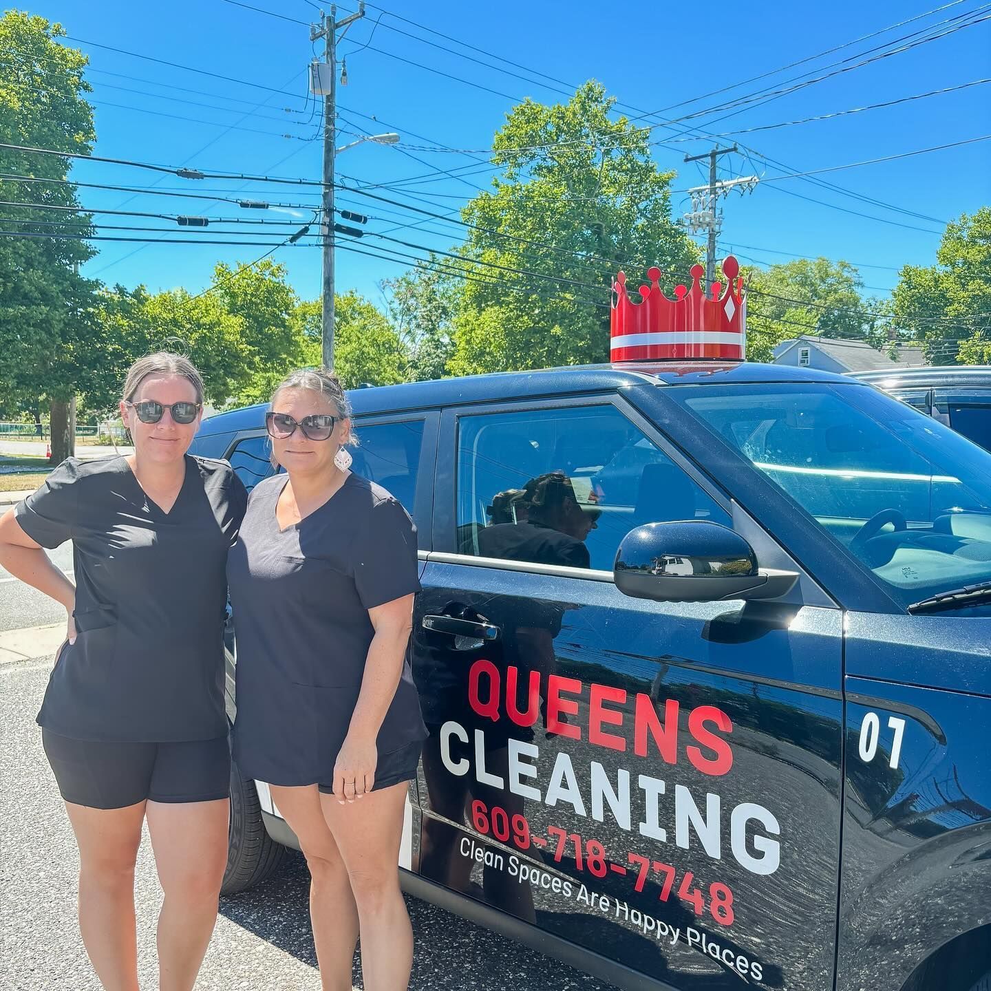 Two women are standing in front of a queens cleaning car.