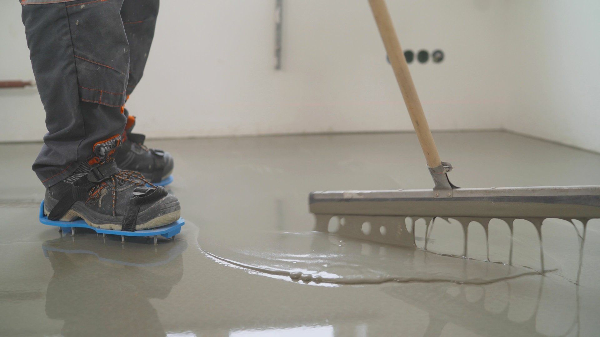 Construction workers in industrial hall applying grey epoxy resin to the floor to create a smooth and durable surface.