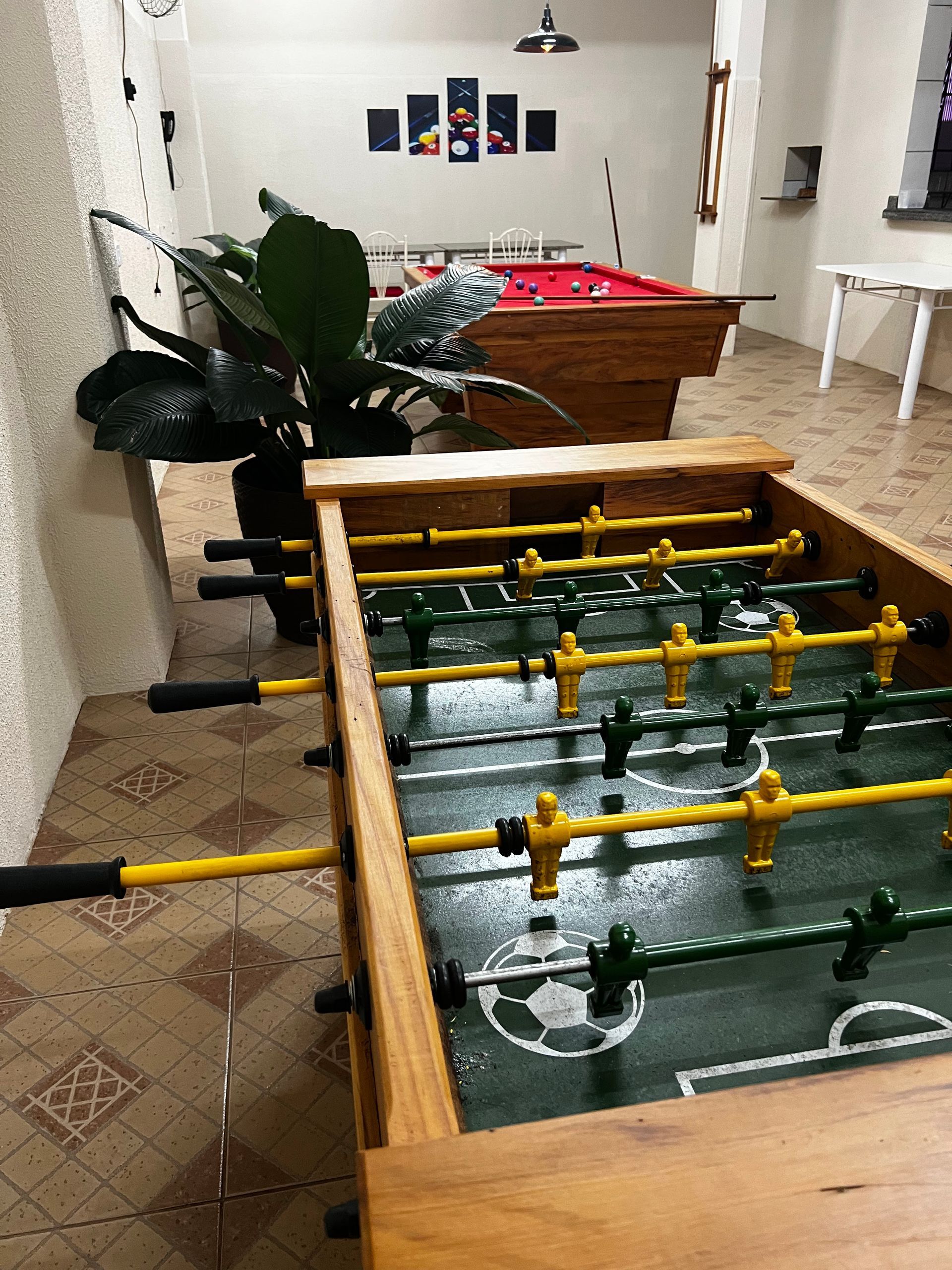 Uma mesa de pebolim está em uma sala ao lado de uma mesa de sinuca.