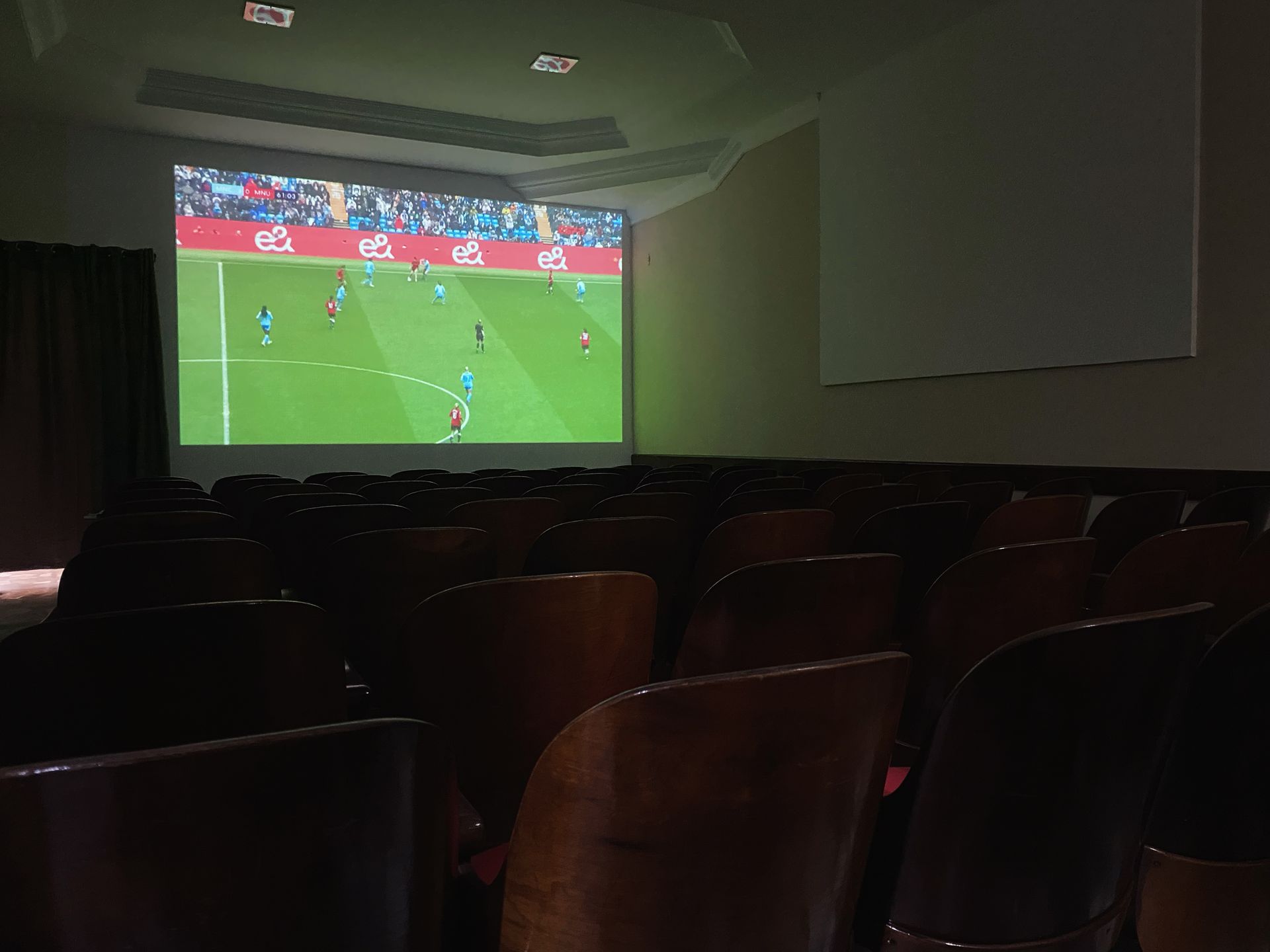 Uma partida de futebol está sendo jogada em uma tela grande em um auditório escuro.