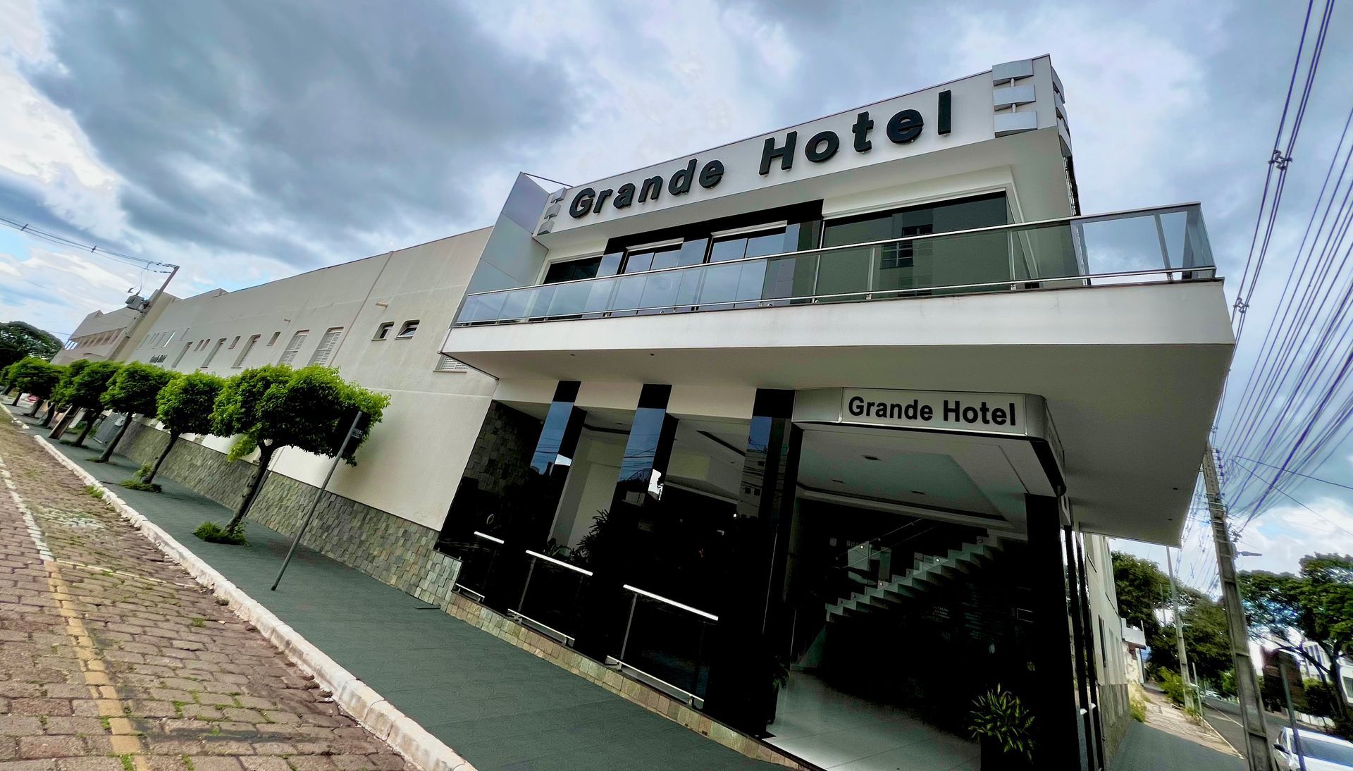 Um grande hotel branco com uma varanda e árvores na frente.