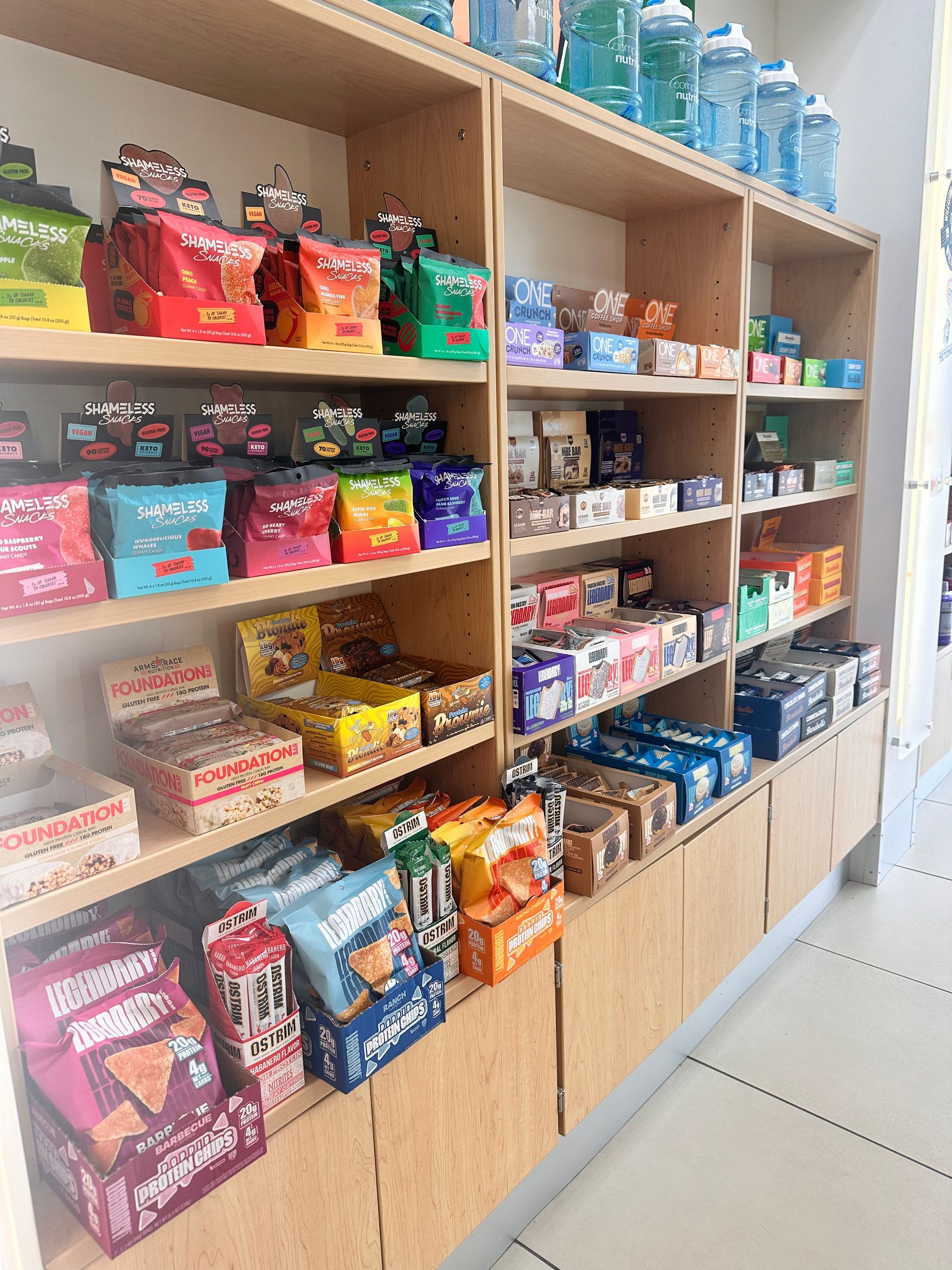 Shelves stocked with various snacks and drinks in a store, with water bottles on the top shelf.