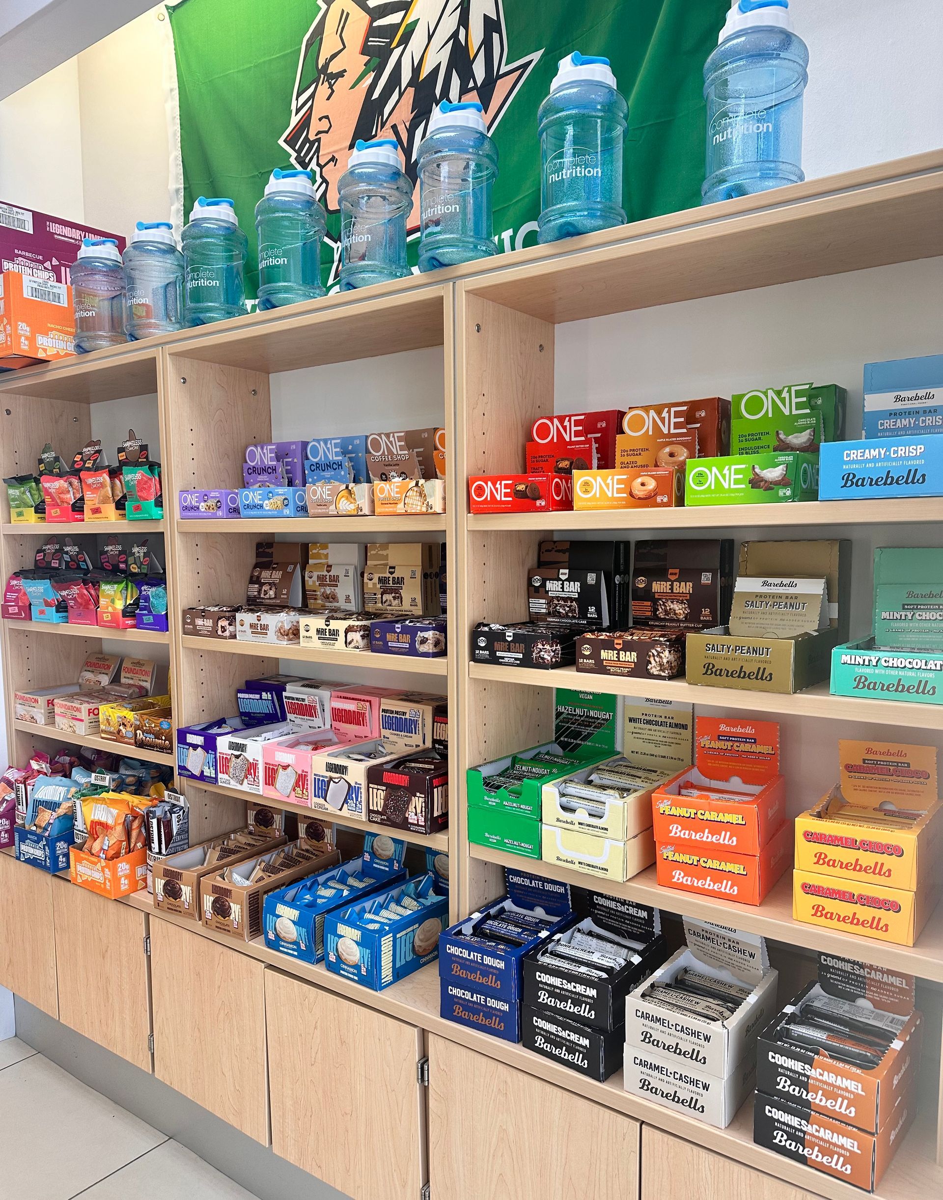 Shelves stocked with various snacks, beverages, and bottled water; green tiger flag in the background.