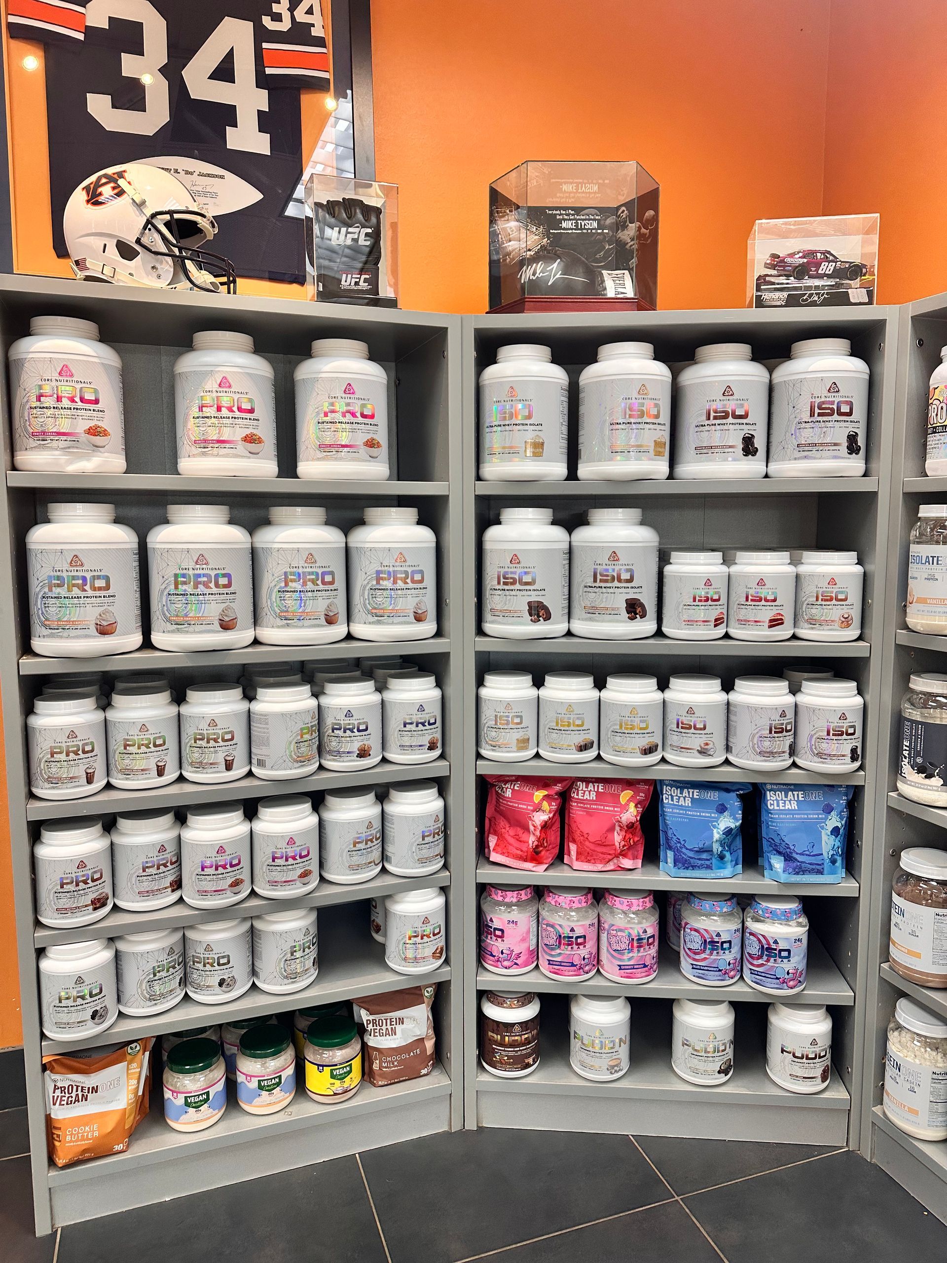 Shelves filled with various white supplement containers, displaying colorful labels, in a sports-themed setting.