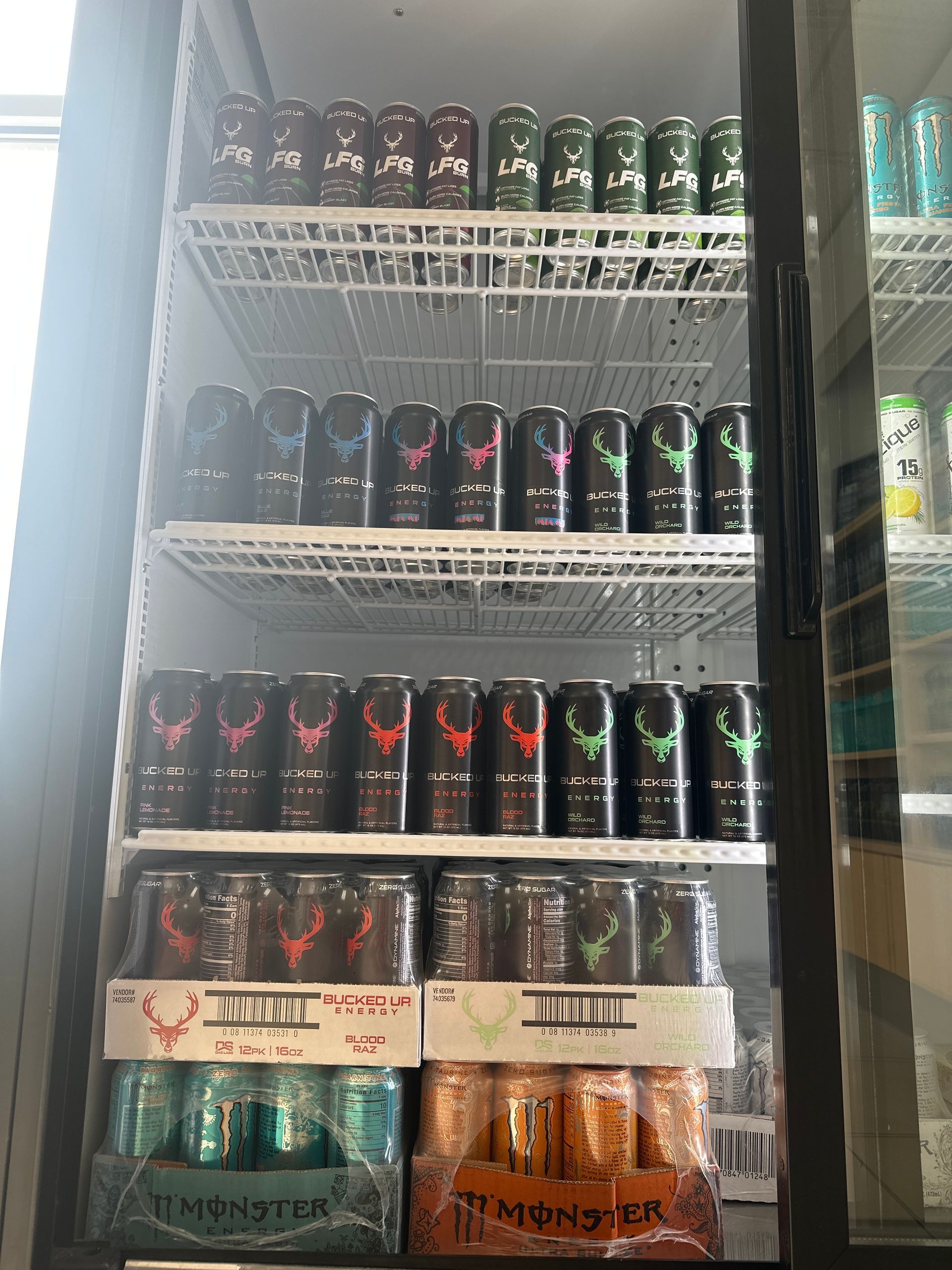 A refrigerated display case filled with various Monster energy drink cans in a store.