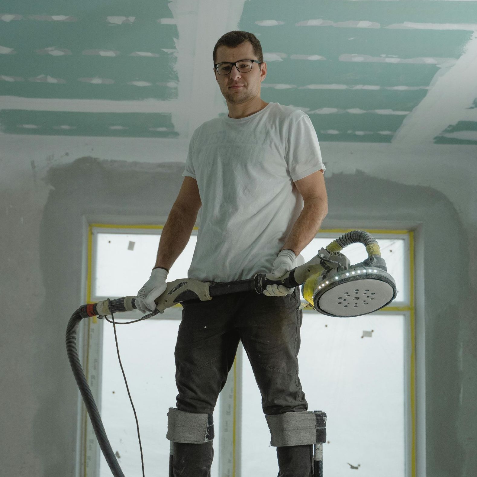 A man is standing on a ladder holding a sander
