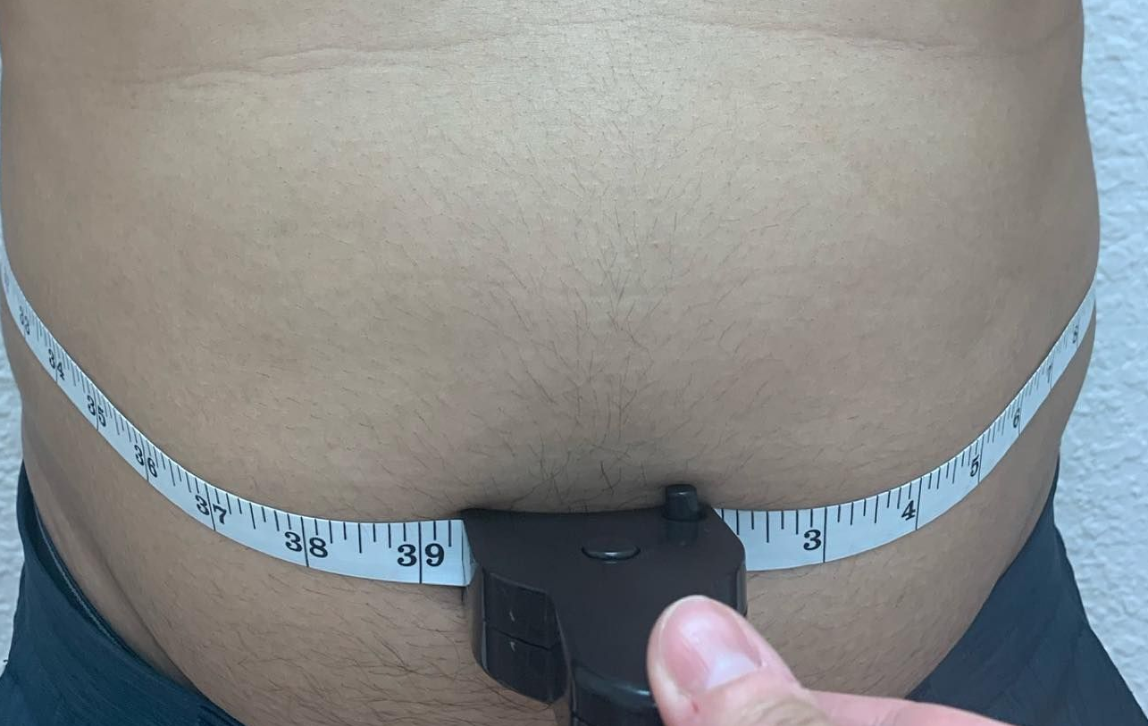 Measuring tape wrapped around a bare waist, with a hand holding the tape measure clasp.