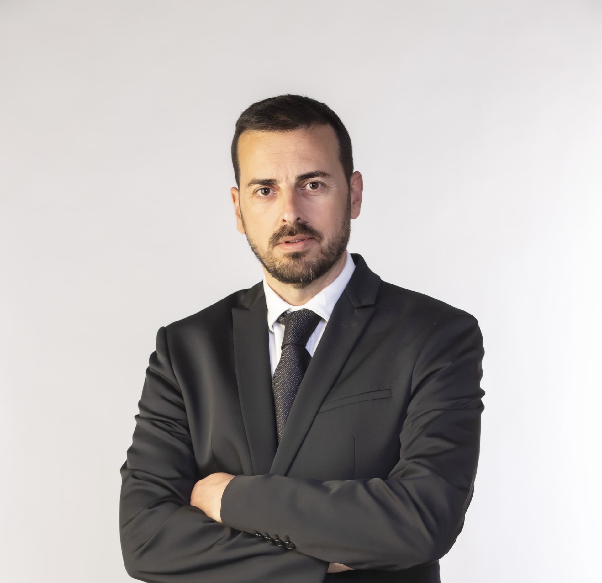 Un hombre con traje y corbata está de pie con los brazos cruzados.