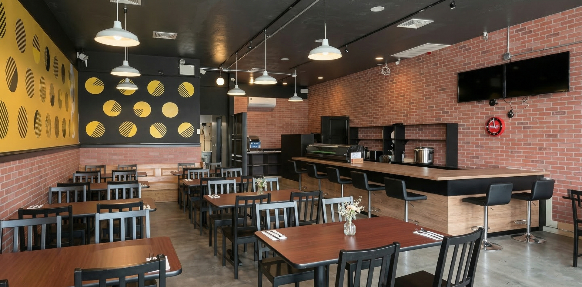An empty restaurant interior with brick walls, black ceilings, wooden tables, and a bar with black stools.
