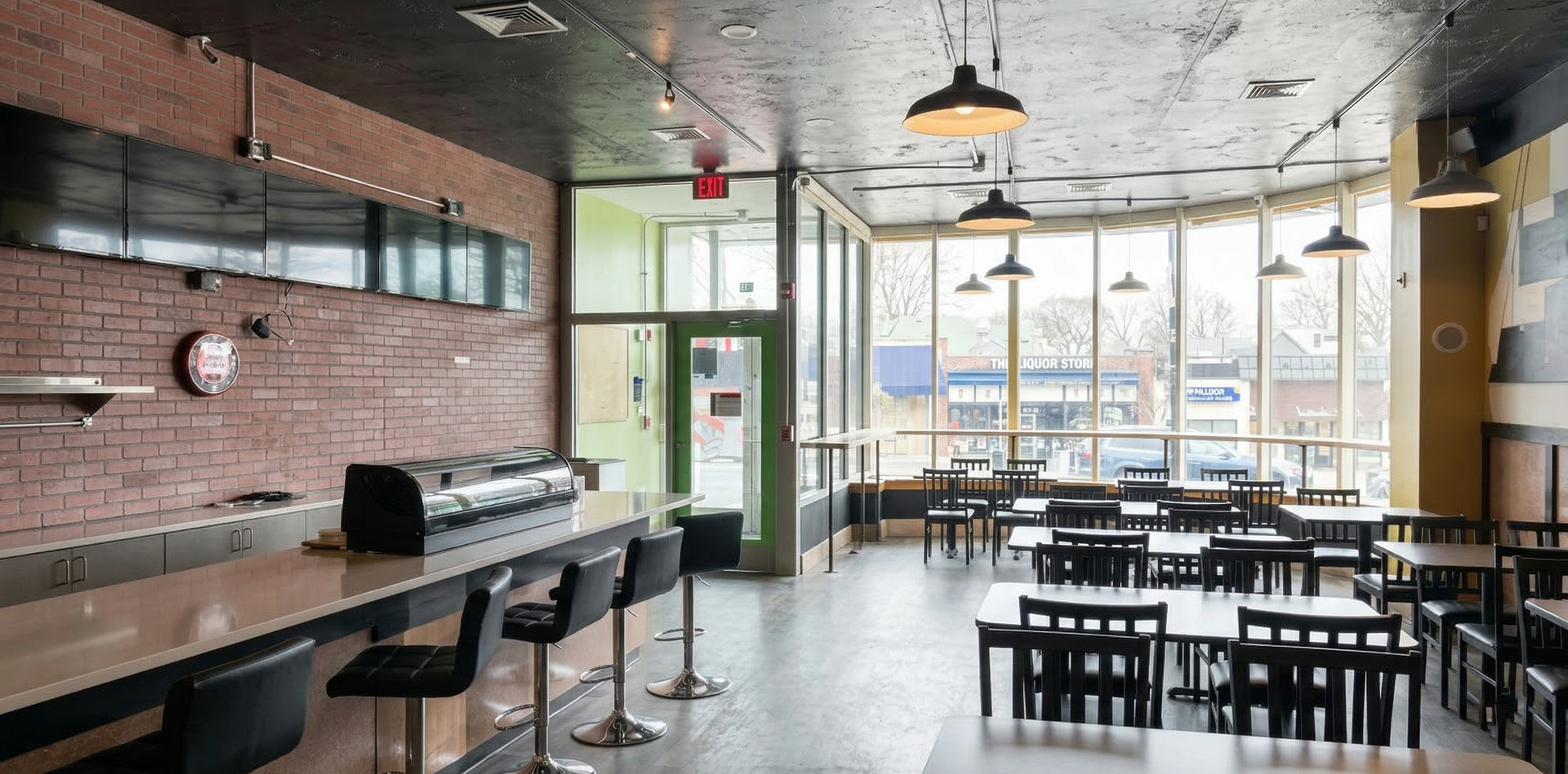 A restaurant interior with a brick wall, counter seating, and tables by large windows overlooking a street.