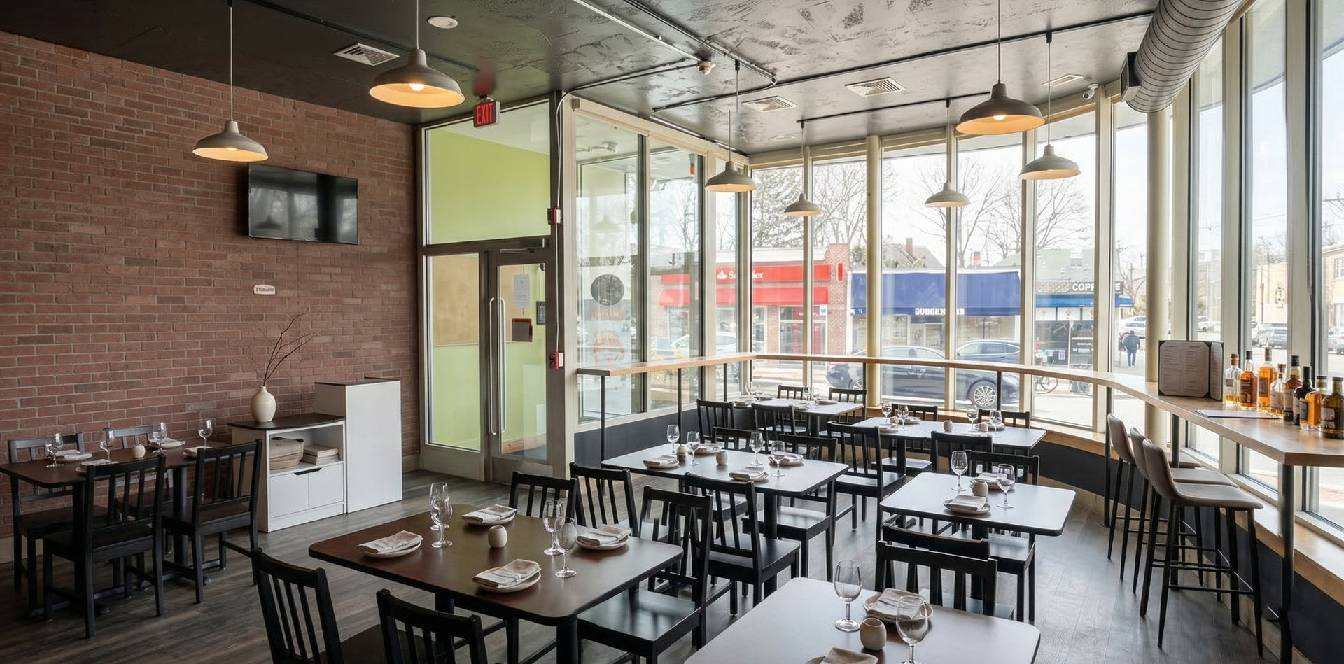 An interior view of a modern restaurant featuring exposed brick walls, dark wood tables, and large windows.