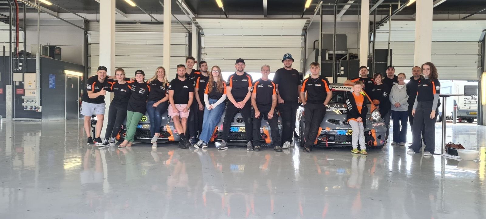 A group of people in team gear standing in front of a race car inside a bright workshop.